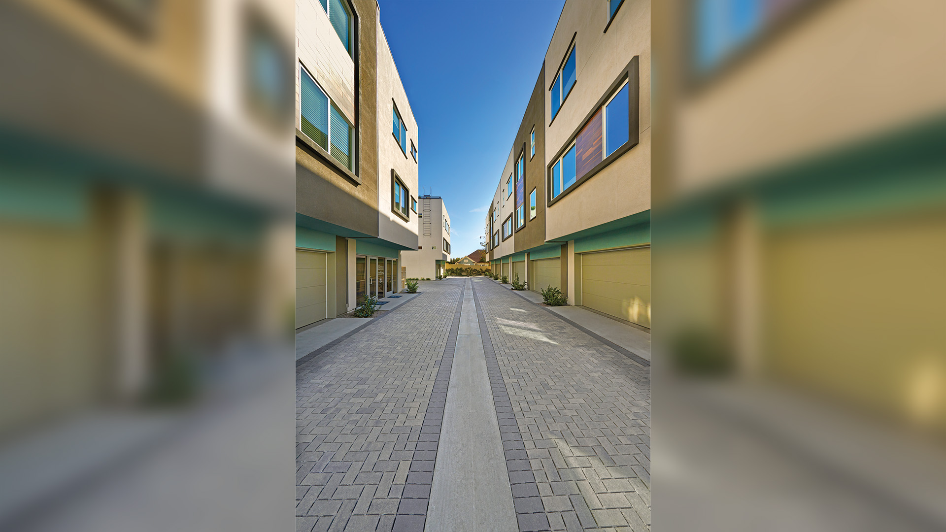 modern housing complex with buildings on left and right and driveway running down the center. driveway is covered in blended gray moss charcoal permeable Holland paving stones installed in a herringbone pattern. solid charcoal permeable Holland paving stones border.