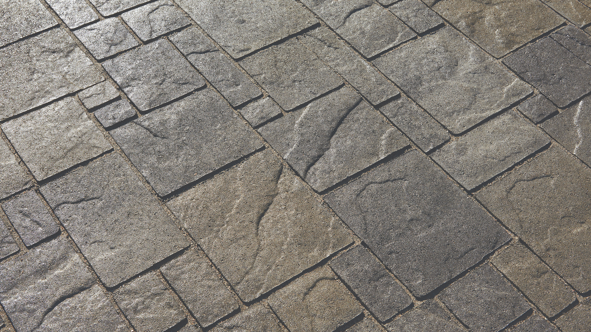 Close-up view of Heartland pavers in a Gray-Moss-Charcoal color blend, installed in a random ashlar pattern. The textured surface features a natural stone appearance with subtle tonal variations, creating a rugged yet refined look ideal for outdoor hardscapes.