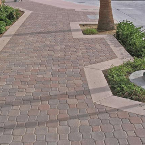 sidewalk with posts, tree, and street on the right. Bushes on the left. sidewalk covered in blended terracotta brown keylock paving stones. sidewalk border is cream brown keylock paving stones.