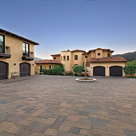 Spacious courtyard paved with a 50/50 field mix of Slate Stone in Sand–Stone–Mocha and Cream–Brown–Charcoal blends, installed in a random ashlar pattern. The setting features a Mediterranean-style estate with warm stucco walls, terracotta roof tiles, and a central water fountain.