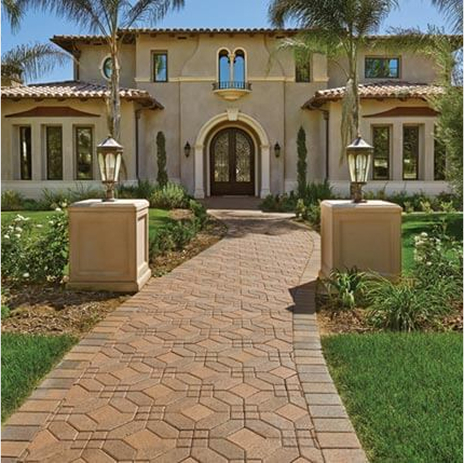 A slightly curved walkway up to custom built home with light tan exterior with dark brown clay roofing. Walkway is covered in symetry 6 by 6 venetian parquet paving stones.