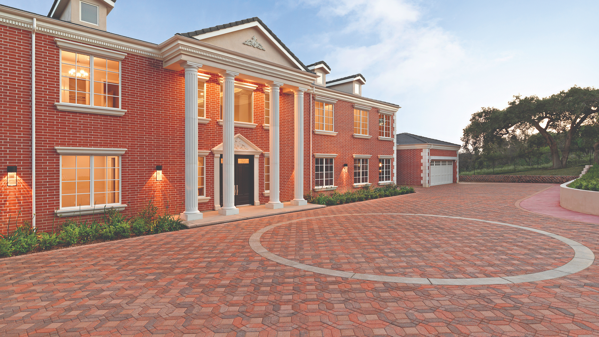 Elegant brick-front estate with a spacious driveway paved in Cream-Terracotta-Brown Symetry® pavers installed in a Venetian parquet pattern, accented by Solid Cream 6x6 pavers forming a circular design.