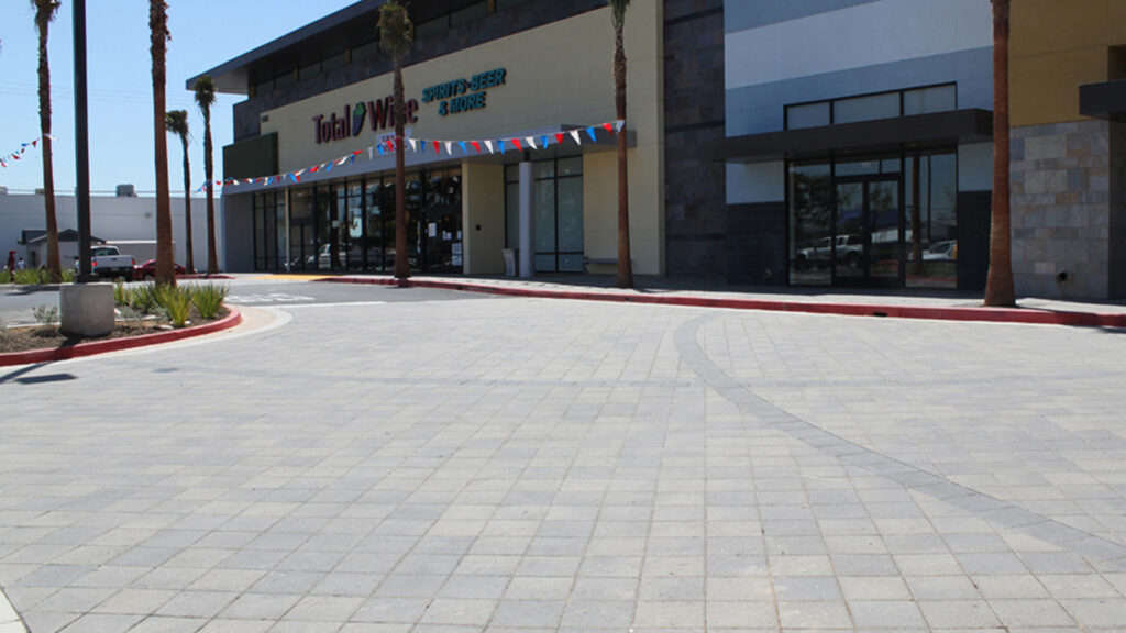 Shopping center entry with Moss-Charcoal 12x12 square pavers installed in a stack bond pattern. The light gray paving stones with subtle charcoal variation form a clean, geometric layout in front of the Total Wine & More storefront.