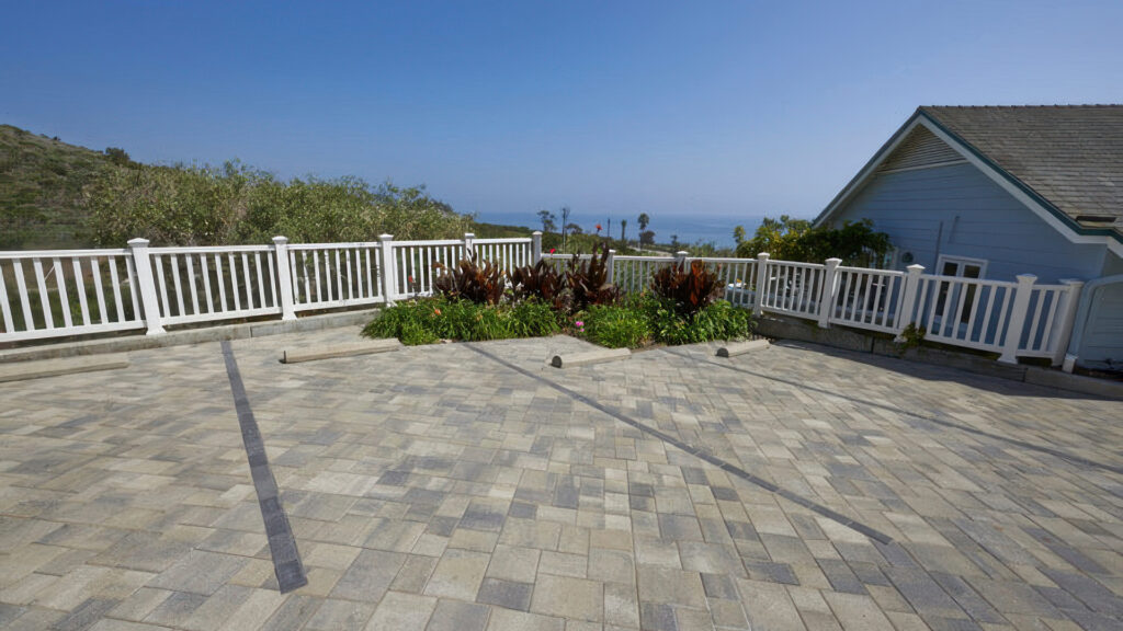 Ocean-view parking area paved with 80mm Courtyard Stone in an ashlar pattern using Gray-Moss-Charcoal color. Parking stall lines are clearly defined with 80mm Holland pavers in solid Charcoal, complementing the overall pattern and layout.