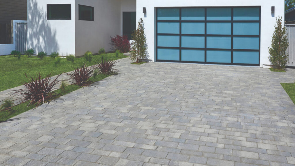 Modern driveway paved with Aqualina paving stones in a Dark Gray–Pewter–Charcoal blend, installed in a random runner pattern. Contemporary white home with frosted glass garage door and minimalist landscaping.
