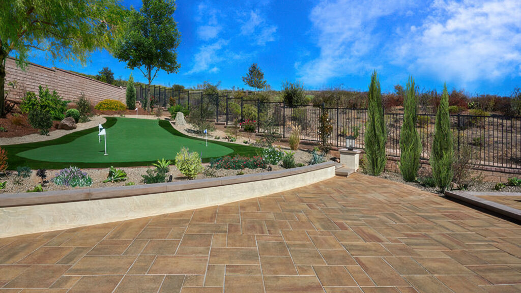 Backyard putting green surrounded by desert landscaping and a black metal fence. In the foreground, a spacious patio is paved with Paseo I and II pavers in Sand-Copper-Stone, laid in a random ashlar pattern. The warm-toned pavers contrast with the green artificial turf and drought-tolerant plants, creating a low-maintenance, elegant outdoor living area.