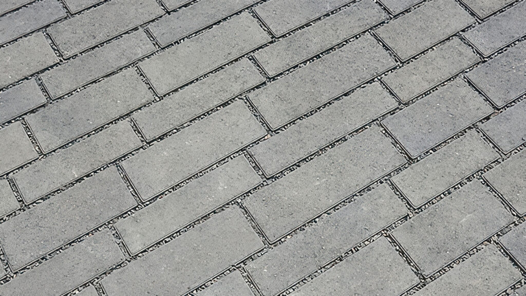 Close-up view of Permeable Aqualina pavers installed in a running bond pattern with rock chips in the joints, designed to allow water infiltration into the open-graded base beneath the pavers.