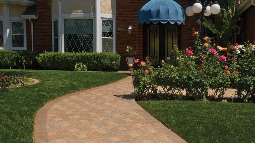 Elegant residential walkway featuring a Venetian parquet pattern using a 50/50 blend of Cream-Brown-Terracotta and Cream-Brown-Charcoal Symetry® pavers, paired with solid Cream 6x6 pavers. The border is a soldier course of solid Brown Holland stone (special order), curving through a manicured lawn and rose garden in front of a classic brick home.