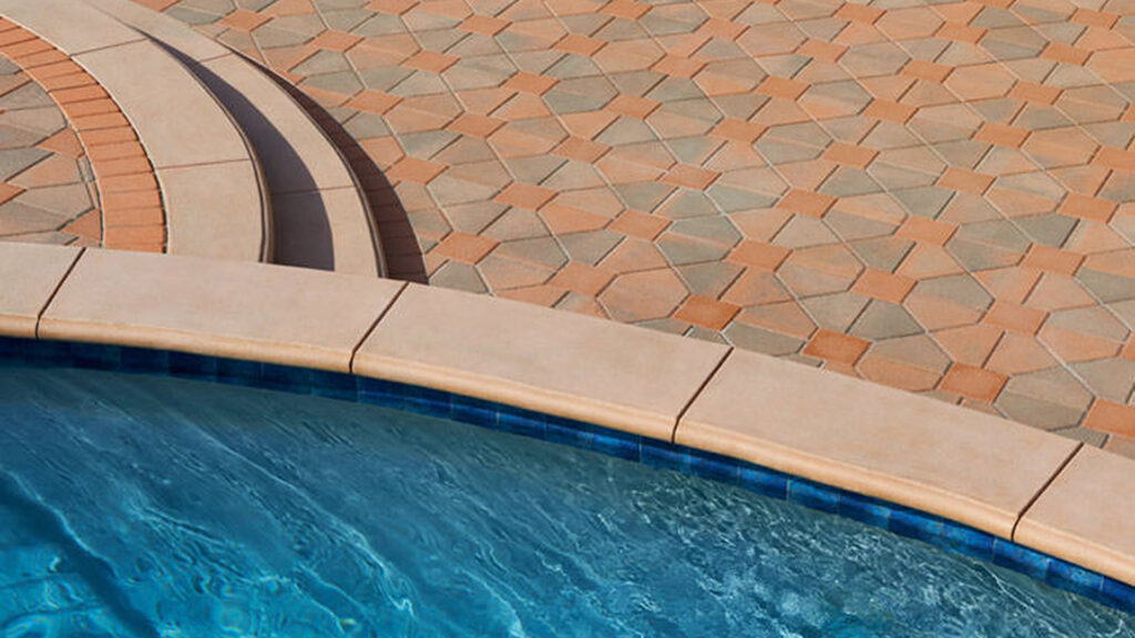 Poolside patio featuring Bishops Hat pavers in Cream-Terracotta-Brown combined with solid Terracotta 8x8s, arranged in a Venetian parquet pattern. The design is framed with a soldier course border of solid Terracotta Antique Cobble I pavers. Light-colored curved coping lines the pool edge, enhancing the geometric tile pattern.