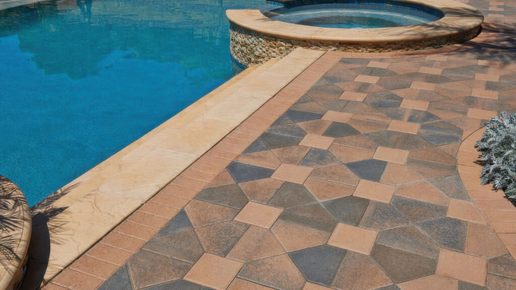 Poolside patio featuring Cream-Brown-Charcoal Bishops Hat pavers combined with Cream 8x8 pavers in a Venetian parquet pattern. The design is bordered with Cream Holland pavers in a soldier course. The space includes curved pool coping in a light tone and a raised spa with stacked stone facing, surrounded by lush landscaping and decorative foliage.