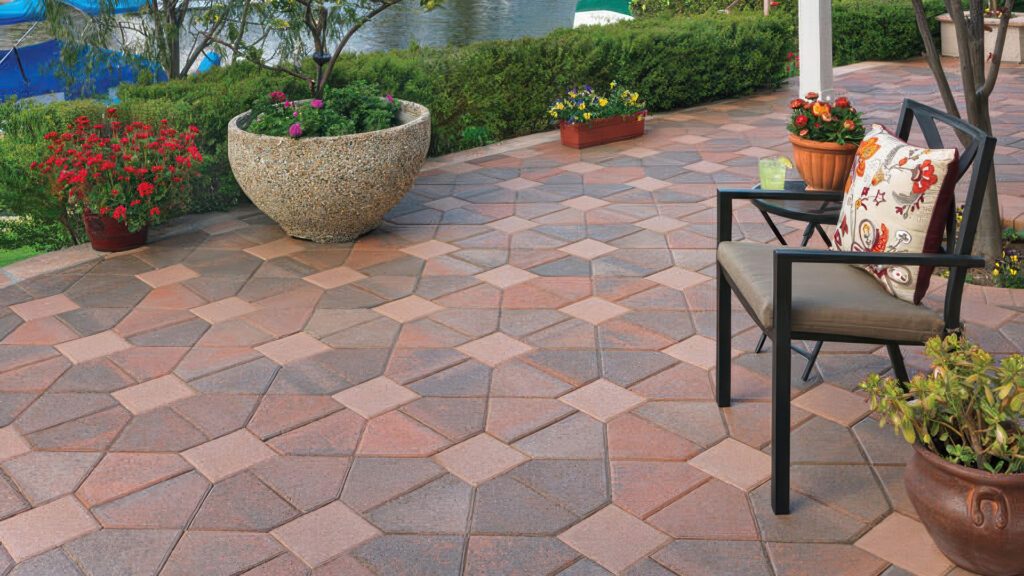 Outdoor patio featuring Cream-TerraCotta-Brown Bishops Hat pavers with solid Cream 8x8 accent stones installed in a Venetian parquet pattern, surrounded by lush planters and cozy seating overlooking a tranquil waterfront.