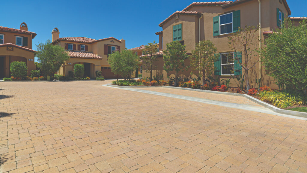 Residential cul-de-sac paved with Sand-Stone Castle Cobble I & II in an ashlar pattern, surrounded by Mediterranean-style homes with clay tile roofs and landscaped with trees and colorful shrubs.