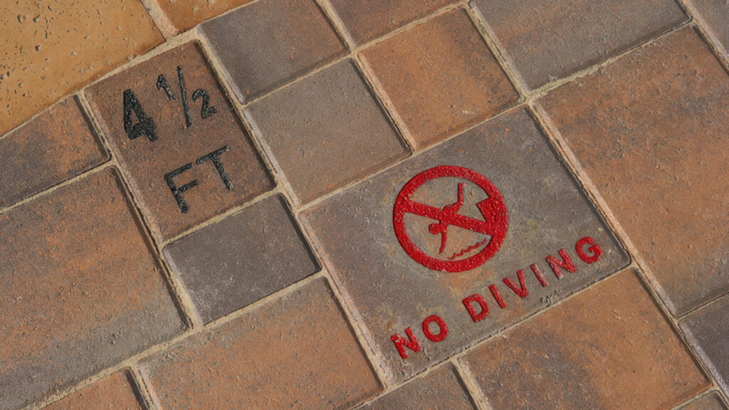 Close-up view of a Courtyard Stone ashlar pattern pool deck in Tuscan color, featuring etched and epoxied "4½ FT" depth marking and "No Diving" symbol. This HOA pool project uses Colorstone technology to reduce maintenance.