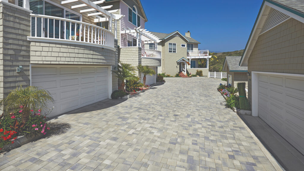 Driveway paved with Gray-Moss-Charcoal blend Courtyard Stone in an ashlar pattern, manufactured at 80mm thickness to accommodate HOA site conditions and expected traffic loads. The design enhances the coastal-style homes with a durable and elegant surface.