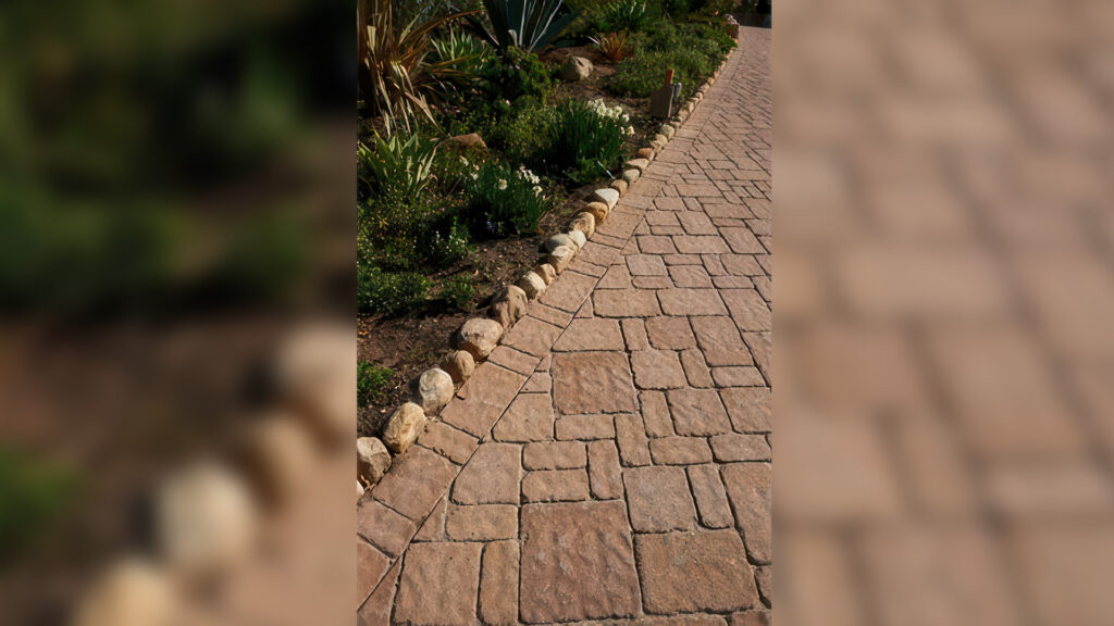 Walkway features Estate Cobble I and II (tumbled) in a Sand-Stone (special order color) installed in an ashlar pattern. The edge border uses tumbled Estate Cobble I in a random runner layout, complemented by a natural stone curb along the garden bed.