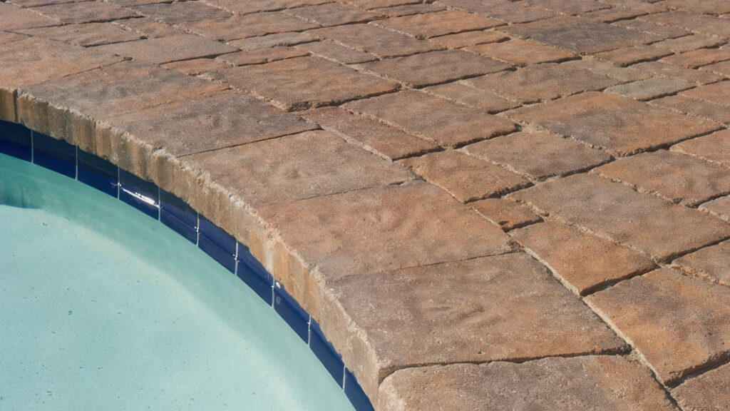 Tuscan tumbled Estate Cobble I and II pavers installed in an ashlar pattern around a pool. Pool coping features matching Tuscan tumbled Estate Cobble II with a natural, textured finish.