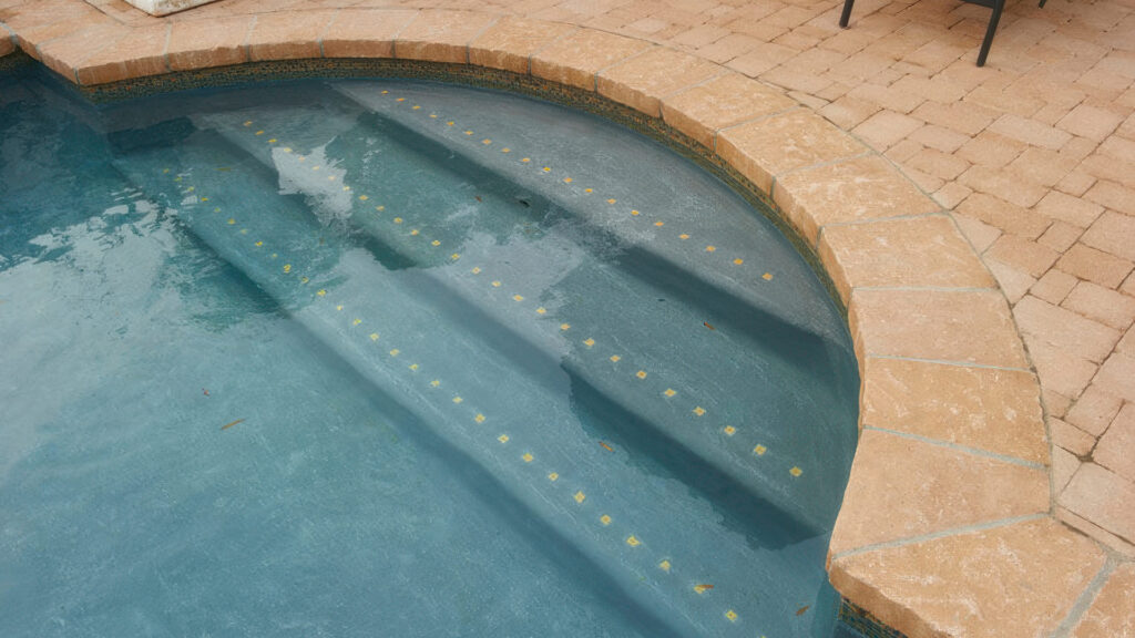 Close-up of a pool entry with Estate Cobble II (tumbled) in Sand-Stone used for the coping. The surrounding paver field features tumbled Sand-Stone Castle Cobble I and II installed in an ashlar pattern, creating a soft, rustic edge around the pool.