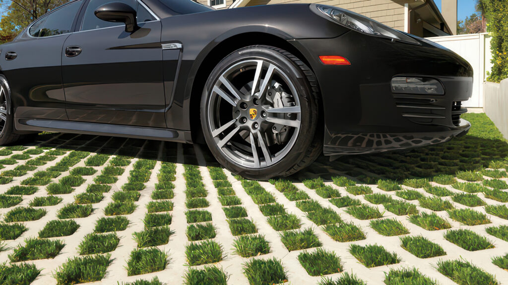 Close-up of a driveway paved with Gray Turfstone filled with artificial turf, creating a greenbelt appearance ideal for areas requiring low maintenance and reduced water use. A luxury black sports car is parked on the surface.
