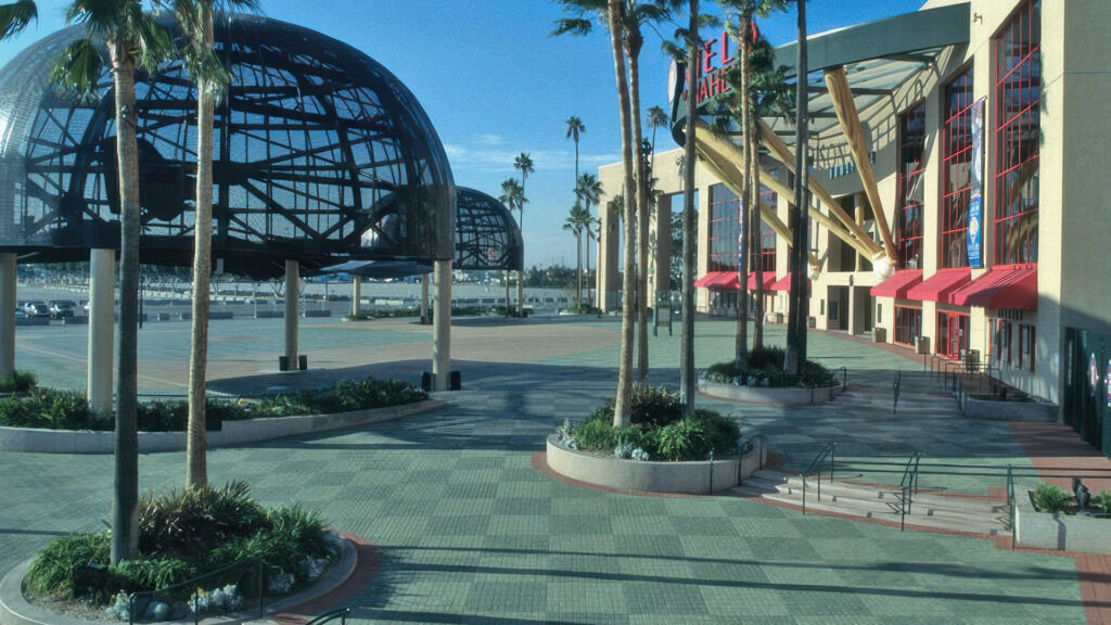 Plaza outside Edison Field in Anaheim, featuring tall palm trees, large helmet sculptures, and bold architectural elements with oversized baseball bats at the entrance. The ground is paved with Holland pavers in Cream and Gray, enhanced by custom colors including Dark Red, Dark Green, Light Green, Gold, Light Gold, and Burgundy. The checkerboard pattern extends throughout the public space, unifying the design and guiding visitors toward the stadium.