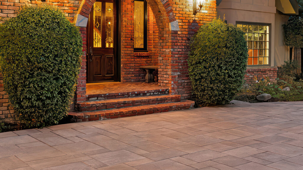 Front entryway paved with Paseo I and II pavers in Adobe–Copper–Mocha blend, installed in an ashlar pattern. The entrance features red brick steps, arched doorway with stained glass, and lush landscaping with neatly trimmed shrubs.