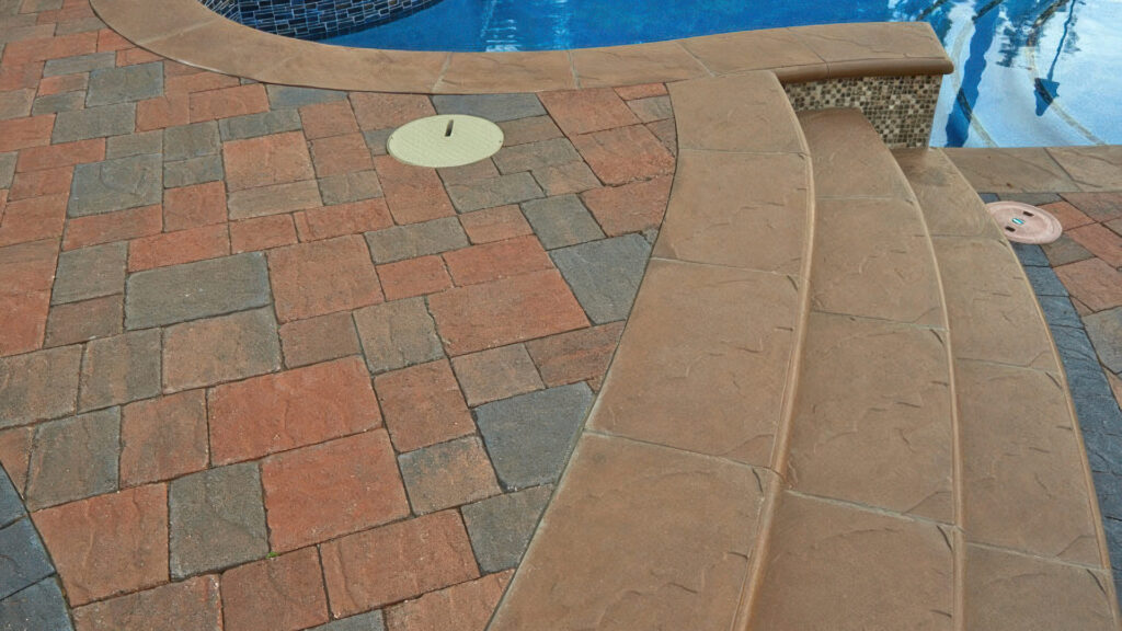 Pool Coping: 50/50 blend of Cream-Terracotta-Brown and Cream-Brown-Charcoal distressed Slate Stone Combo installed in an ashlar pattern. A solid Charcoal 6x9 distressed Slate Stone border outlines the edge, adjacent to smooth textured bullnose pool coping and curved steps leading into the pool.