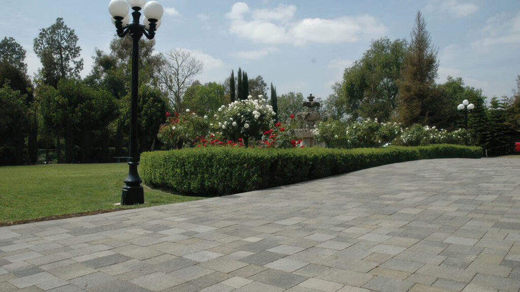 Gray-Moss-Charcoal Slate Stone (distressed) paving installed in an ashlar pattern, forming an elegant walkway beside manicured hedges, blooming red and white roses, and a traditional black lamp post in a lush garden setting.