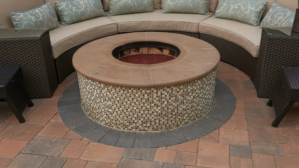 Cozy patio seating area featuring a circular third-party fire pit with a mosaic tile base and smooth bullnose cap. Surrounding pavers are Slate Stone Combo (distressed) in an ashlar pattern, blending a 50/50 mix of Cream-Terracotta-Brown and Cream-Brown-Charcoal tones. The border is made of Slate 6x9 (distressed) pavers in solid Charcoal, adding contrast and definition.