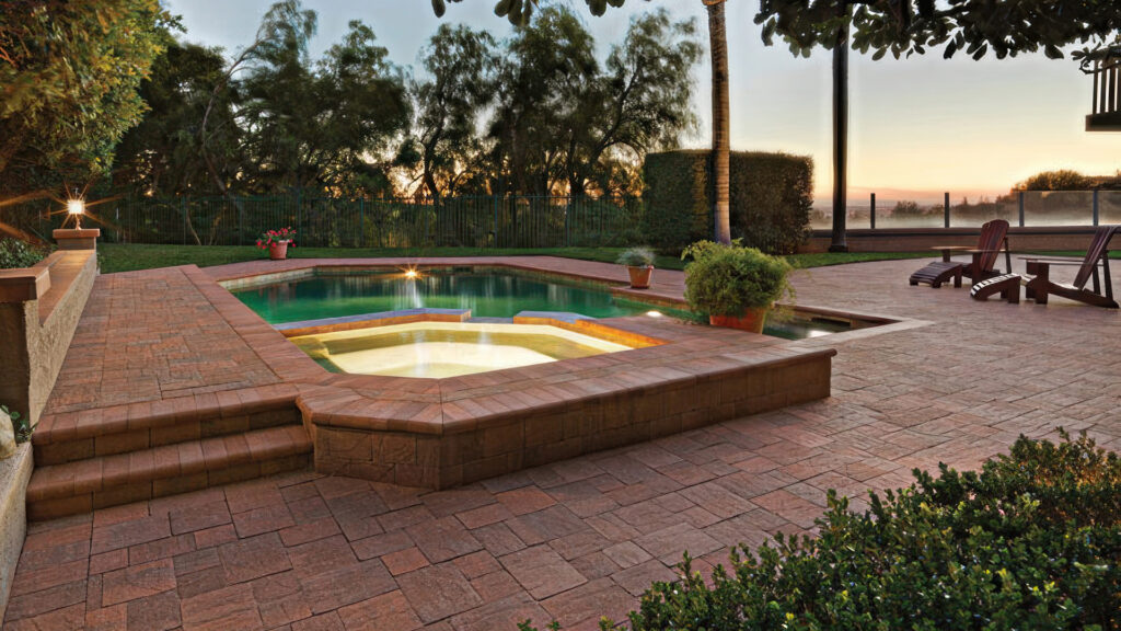 Elegant backyard pool and spa area at sunset featuring Cream-Terracotta-Brown Slate Stone pavers installed in an ashlar pattern. The raised spa and pool edges are finished with matching Cream-Terracotta-Brown bullnose coping. The patio includes built-in planters, steps, Adirondack chairs, and surrounding greenery, creating a peaceful, warm atmosphere.