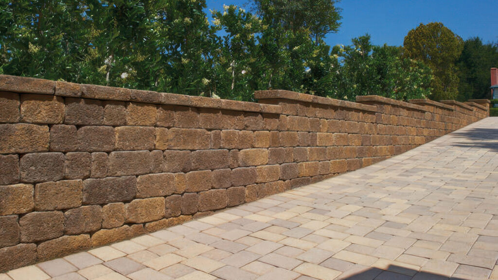 Retaining wall built with Sand-Stone-Mocha Stonewall® II blocks and cap, featuring a decorative stepped design. The adjacent walkway is paved with Sand-Stone-Mocha Antique Cobble I & II pavers arranged in a random ashlar pattern, creating a warm, cohesive outdoor hardscape.