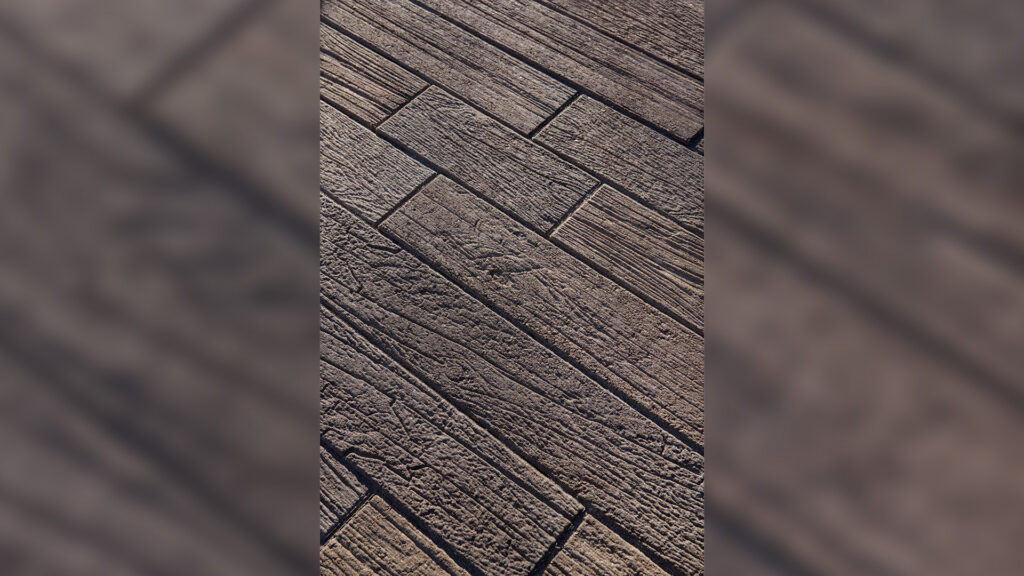 Close-up view of Dark Gray-Copper-Charcoal Timberline pavers showcasing a realistic wood grain texture arranged in a staggered plank layout.