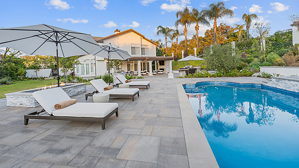 Blended Dark Gray Copper Charcoal Paseo I & II pavers installed in a random ashlar pattern create a spacious pool deck with modern lounge chairs, umbrellas, and surrounding landscaped garden.