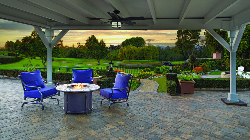 Slate Stone pavers in a Sand, Stone, and Mocha color blend, installed in a random ashlar pattern, create a covered patio overlooking a landscaped garden and golf course. A Slate 6x9 Mocha soldier-course border frames the outdoor living space, which features a fire pit seating area and panoramic sunset views.