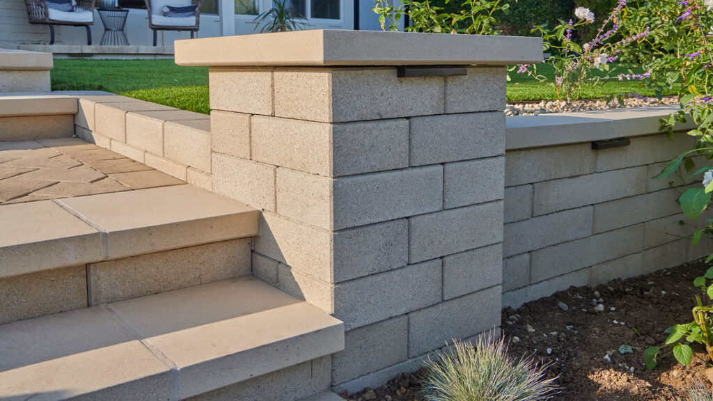 A landscape staircase and retaining wall constructed with gray Bastione Wall Stone™. The column is built with 12-inch Bastione Wall Stone™ in Gray, while the adjoining retaining wall uses 24-inch Bastione Wall Stone™ in Gray installed in a running bond pattern. Smooth concrete stair treads, integrated wall lighting, and surrounding garden plantings complete the contemporary outdoor design.