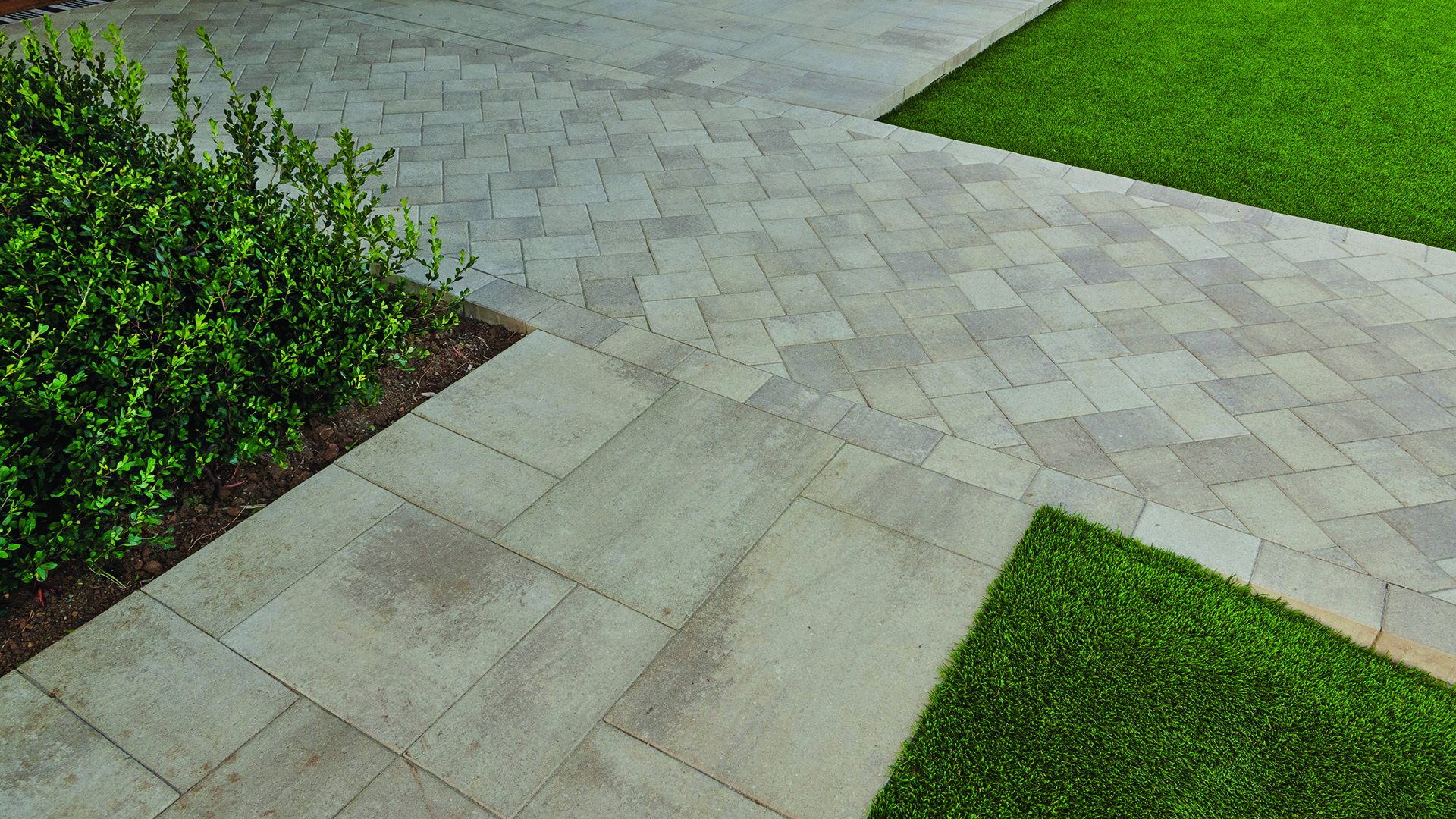 Landscape walkway showcasing Porcellana 6-inch pavers in Light Sand-Gray-Stone installed in a herringbone pattern, bordered by Porcellana 18-inch pavers in Light Sand-Gray-Stone installed in a random ashlar pattern. The light-toned pavers create a clean transition between lawn and planting beds, highlighting the contrasting paving patterns and contemporary outdoor design.