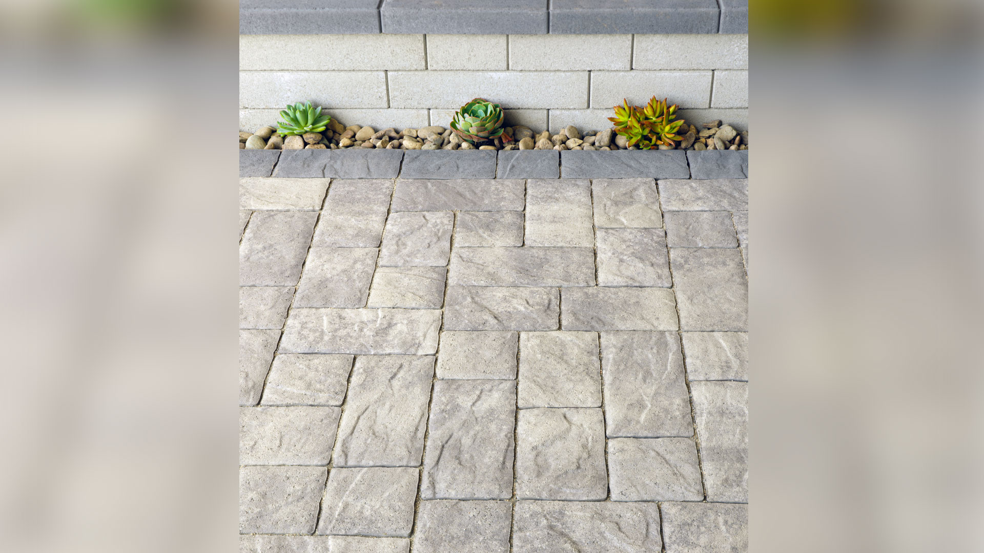 Gray-Charcoal Portofino paving stones installed in a random ashlar pattern with a solid Charcoal random runner border along a raised planter wall.
