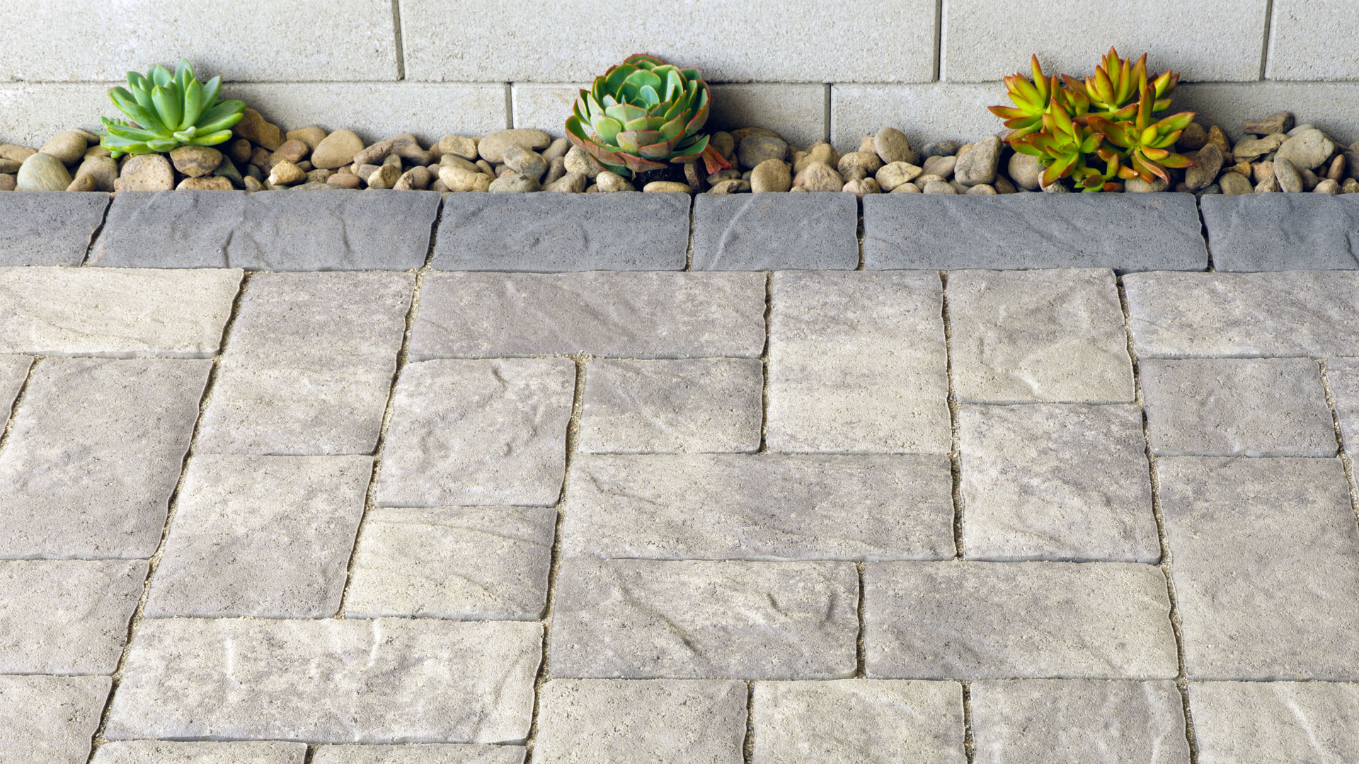 Gray-Charcoal Portofino paving stones installed in a random ashlar pattern with a solid Charcoal random runner border along a raised planter wall.